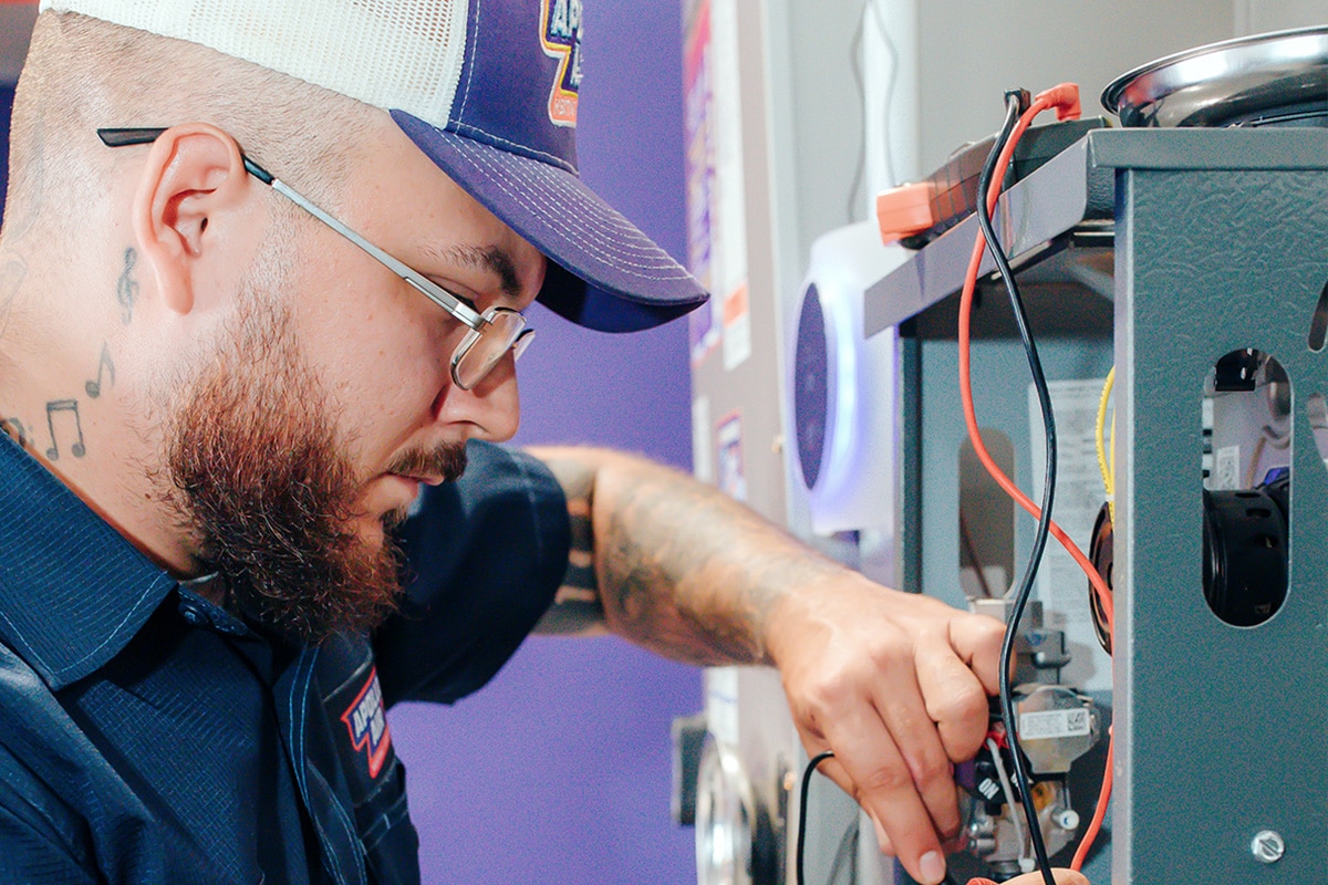 Apollo Air technician Destin focused on connecting wiring to a furnace control board during a residential heating system repair