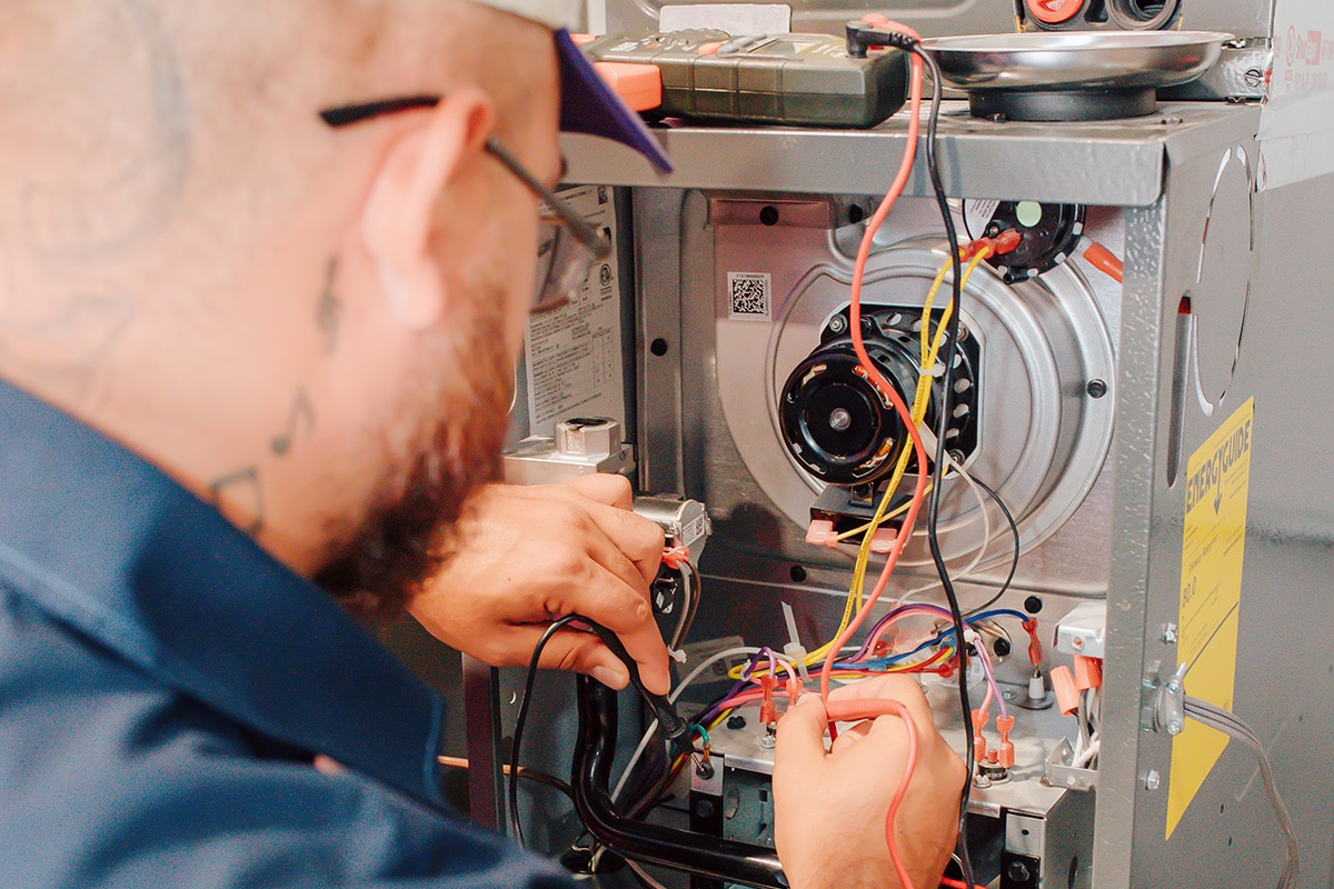 Apollo Air technician Destin focused on connecting wiring to a furnace control board during a residential heating system repair