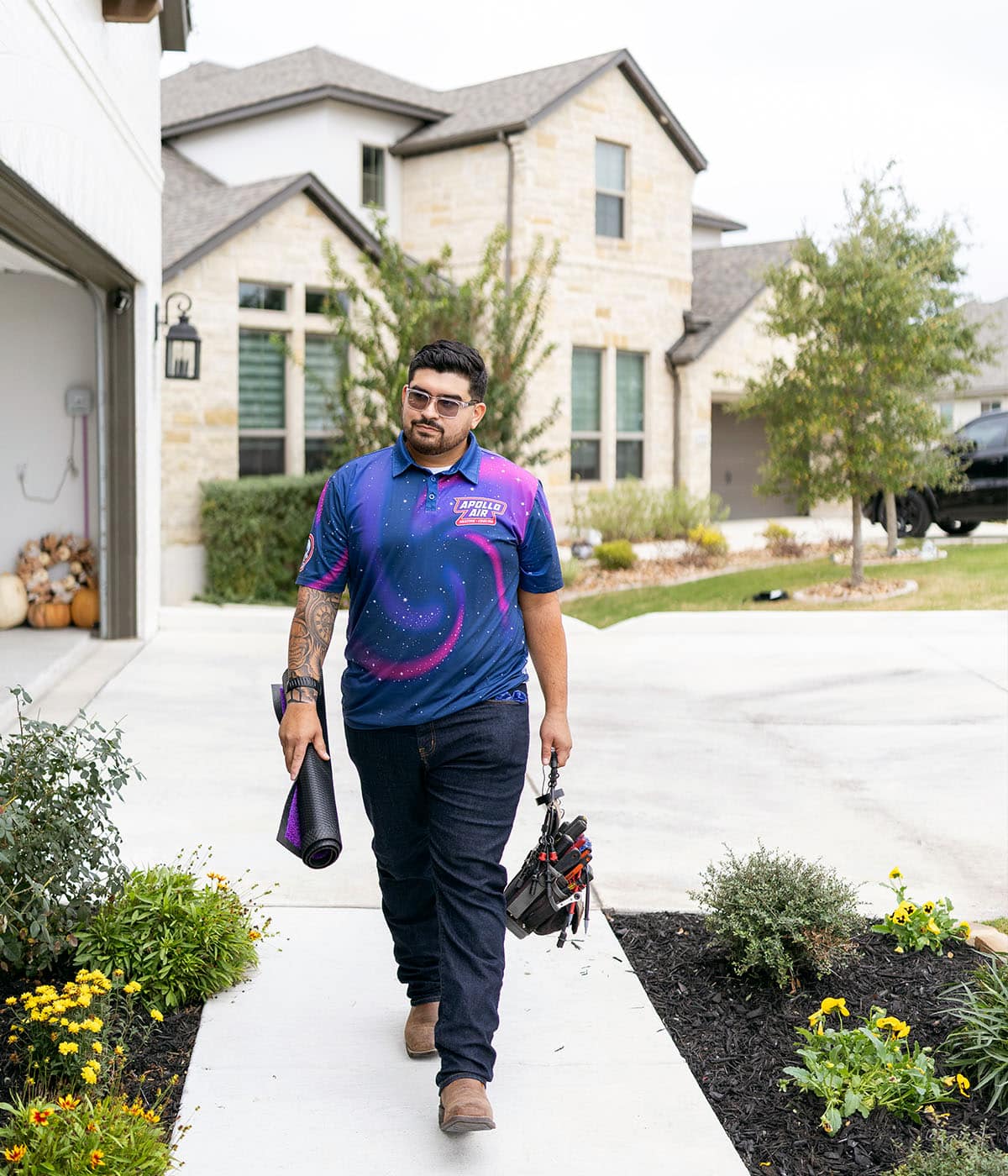 Apollo Air Heating and Cooling technician walking up a residential driveway carrying tools and a mat for an HVAC service call