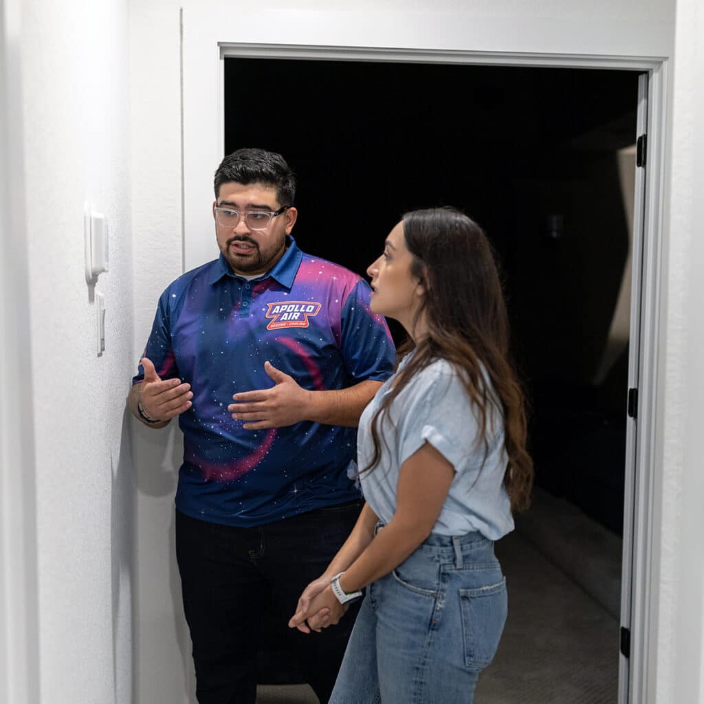 Apollo Air technician discussing HVAC service details with a homeowner in a residential hallway