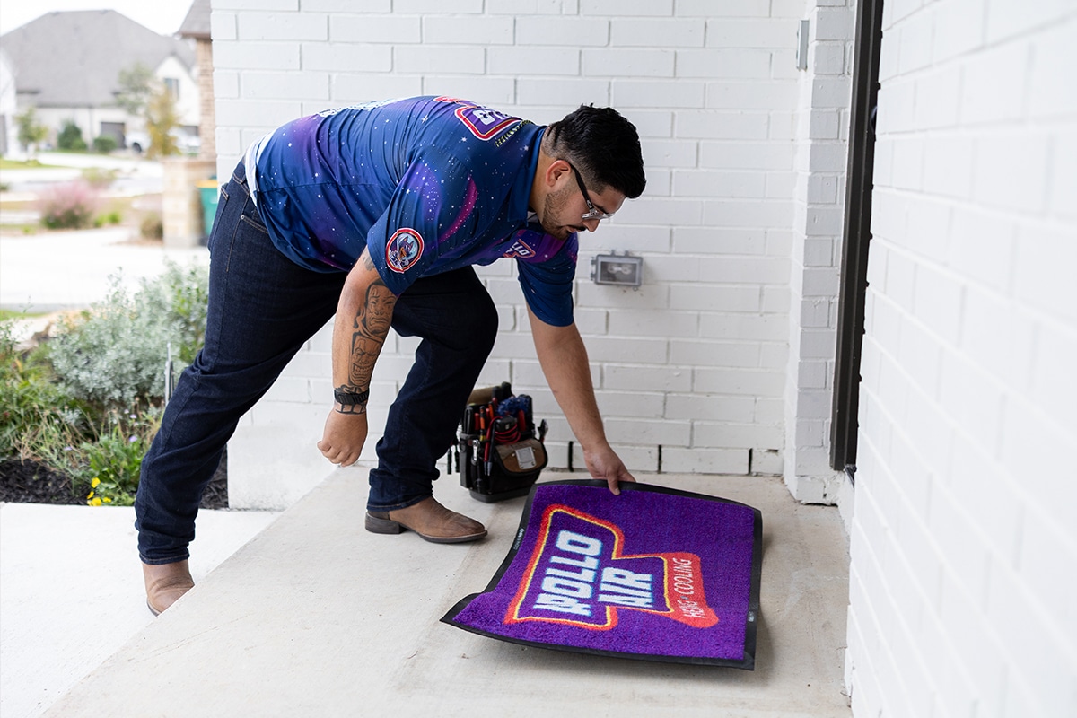 Apollo Air Heating and Cooling technician carefully laying down a branded logo mat at a customer's front door