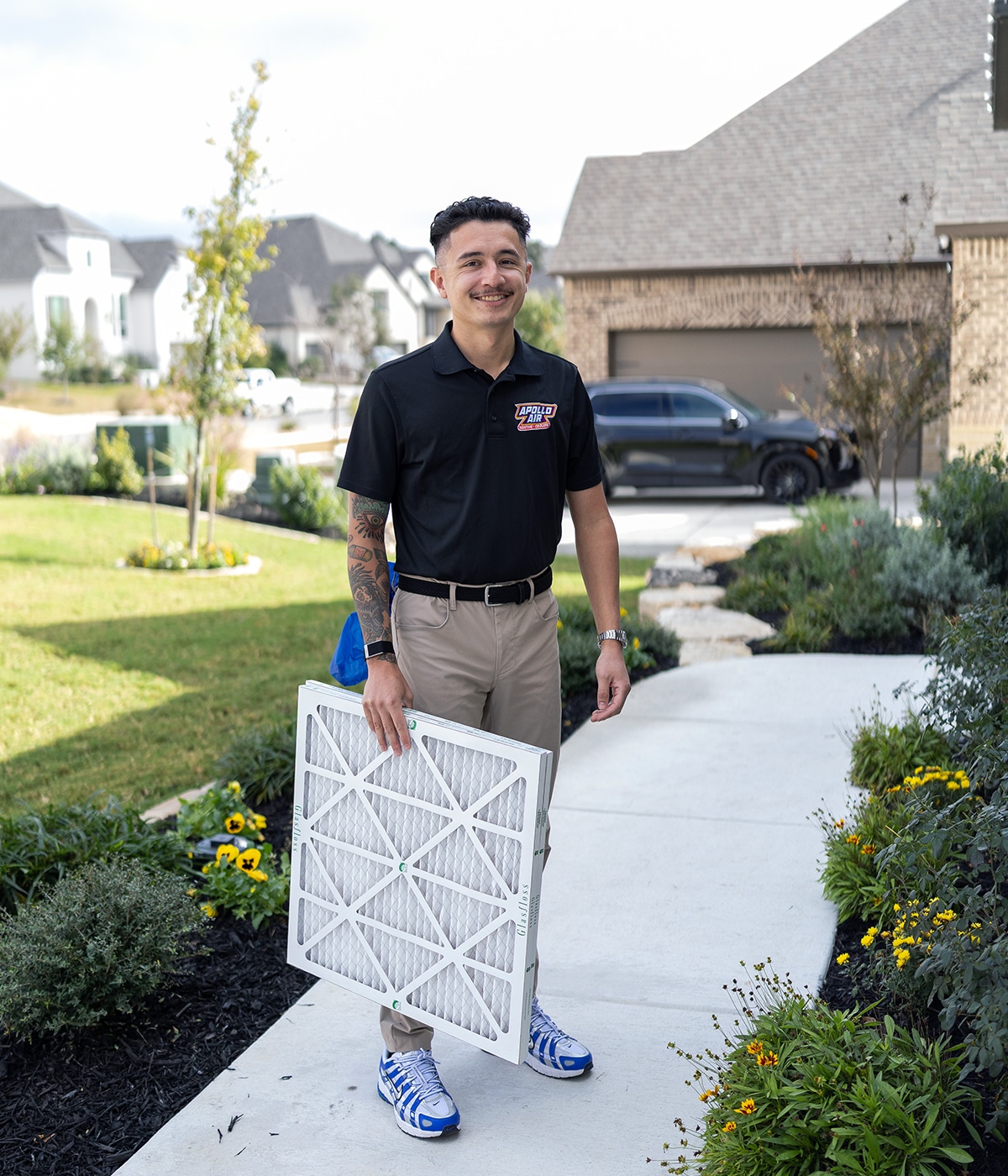 Smiling Apollo Air Heating and Cooling technician holding a new Glasfloss air filter in front of a residential home