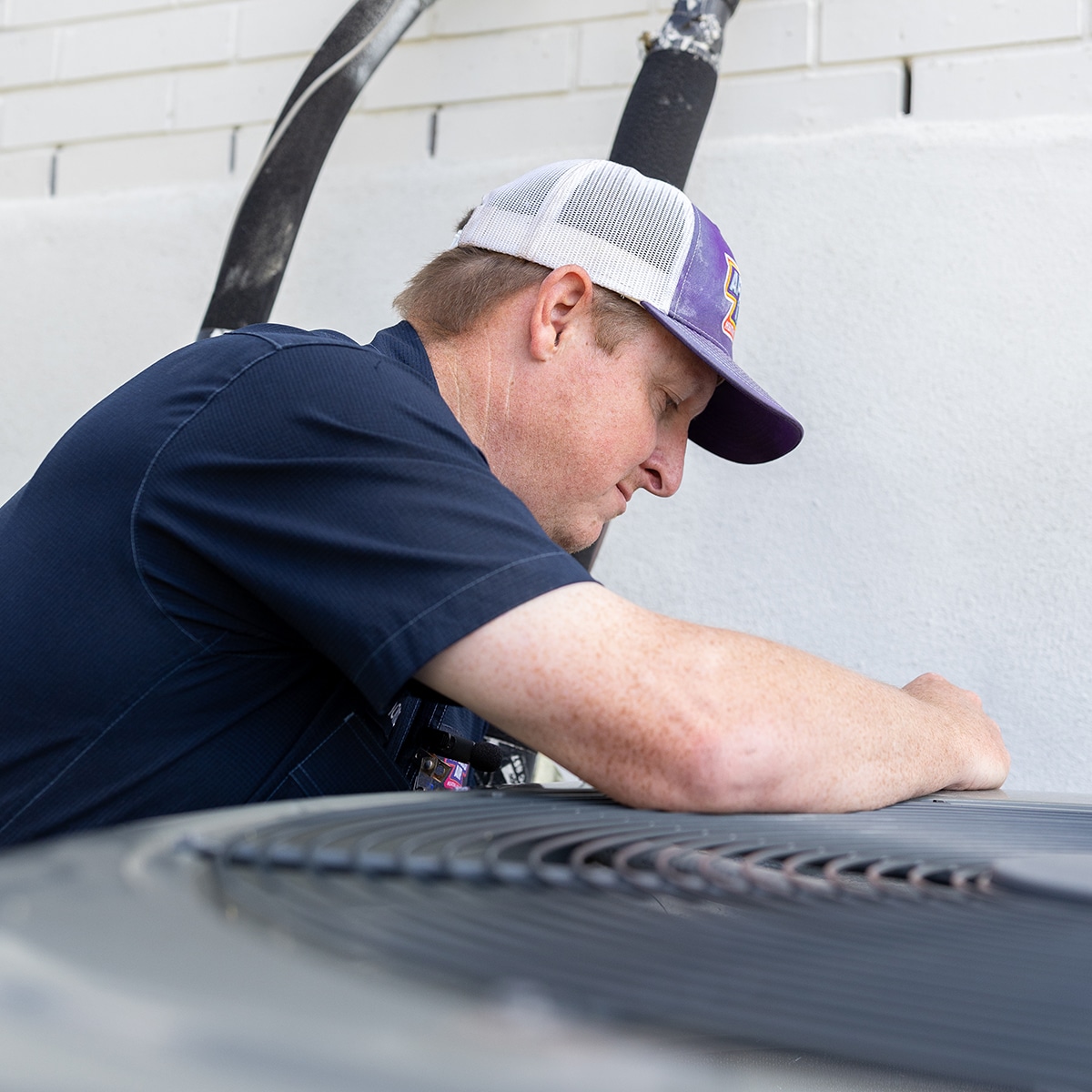 Apollo Air technician Thomas closely inspecting the top of an outdoor AC condenser unit during a residential HVAC service call