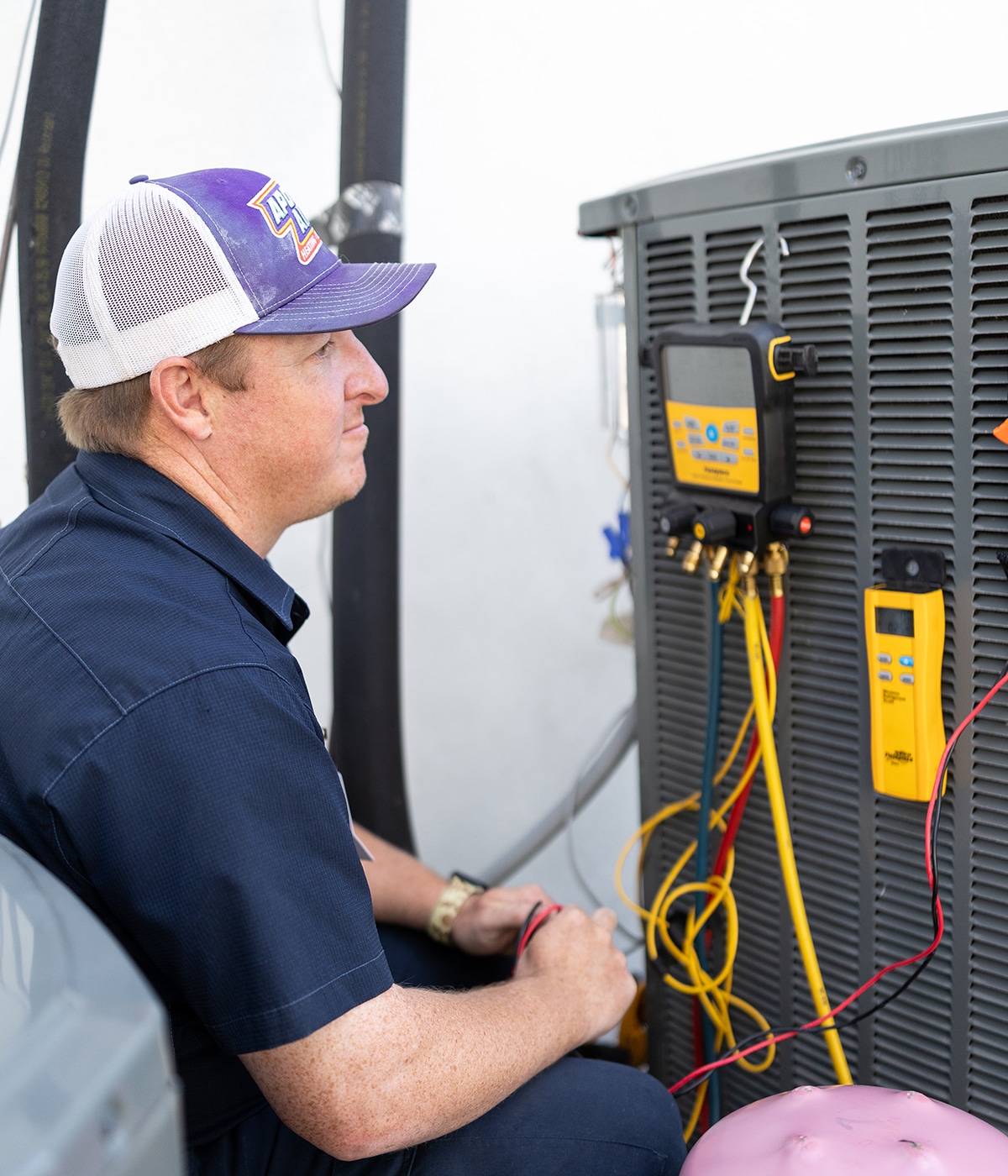 Apollo Air technician Thomas monitoring Fieldpiece refrigerant manifold gauge and thermometer readings on an outdoor AC unit during a service call