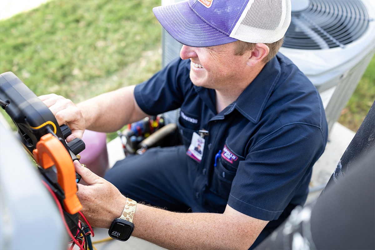 Smiling Apollo Air technician Thomas connecting a clamp meter to an outdoor AC unit during a residential HVAC service call
