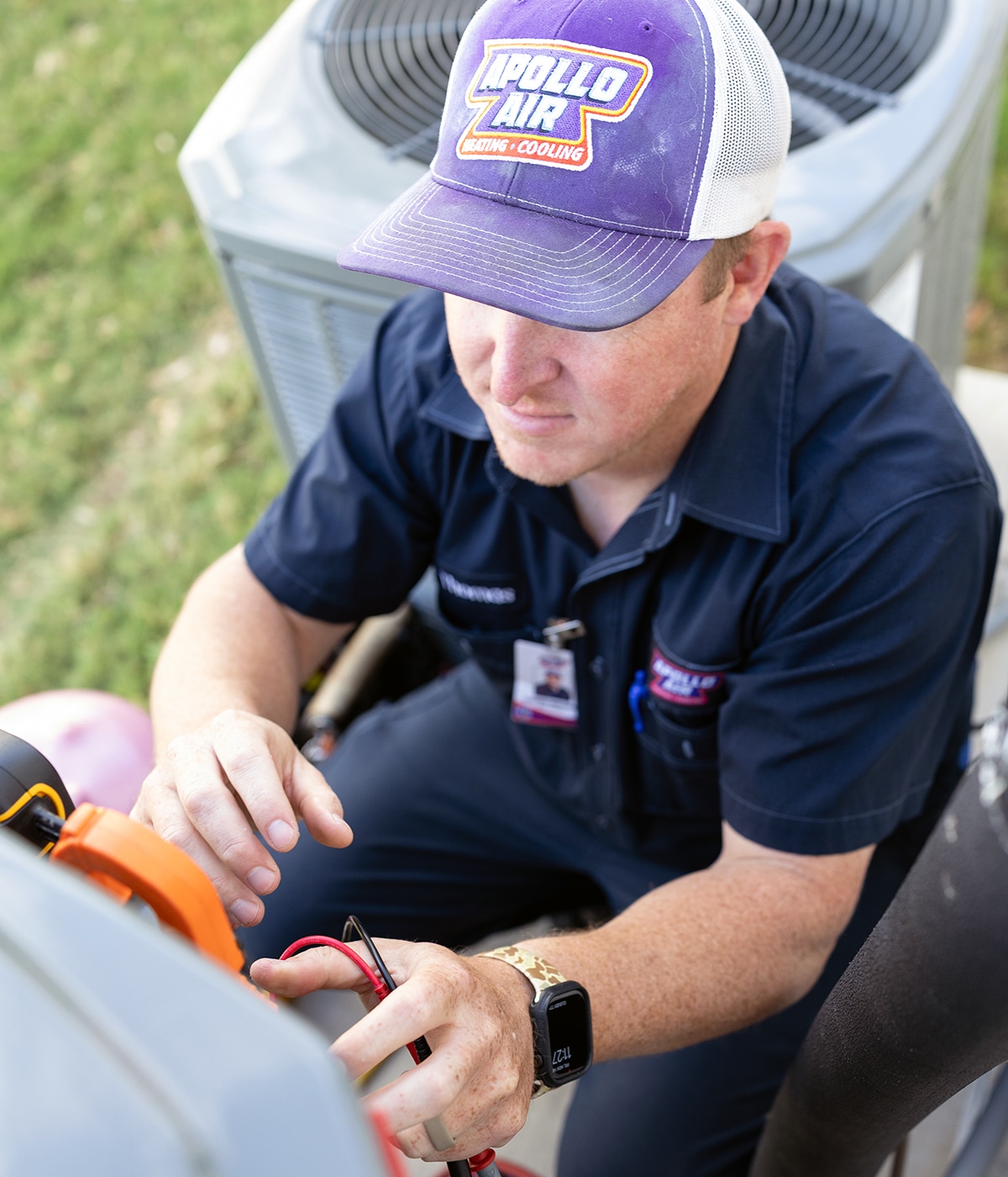 Apollo Air technician Thomas using a clamp meter to test electrical components on an outdoor air conditioning unit