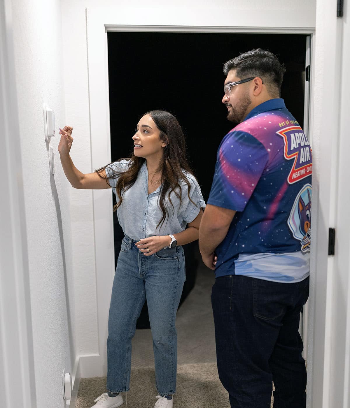 Apollo Air technician explaining smart thermostat features to a homeowner on a residential hallway wall
