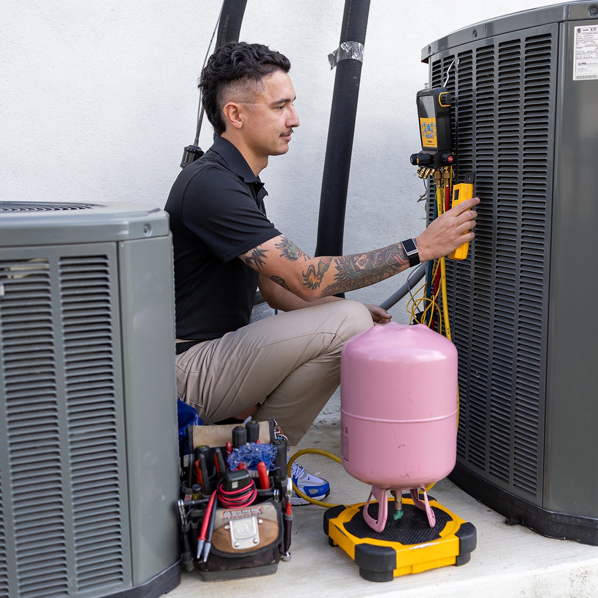 Apollo Air HVAC technician connecting a Fieldpiece refrigerant manifold gauge to a Trane outdoor AC unit with refrigerant tank and tools nearby
