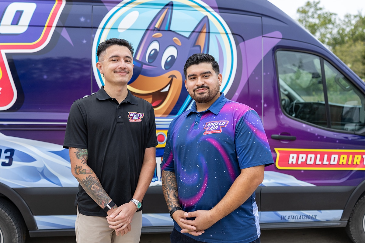 Two Apollo Air Heating and Cooling technicians smiling in front of their branded service van featuring the Apollo Air mascot