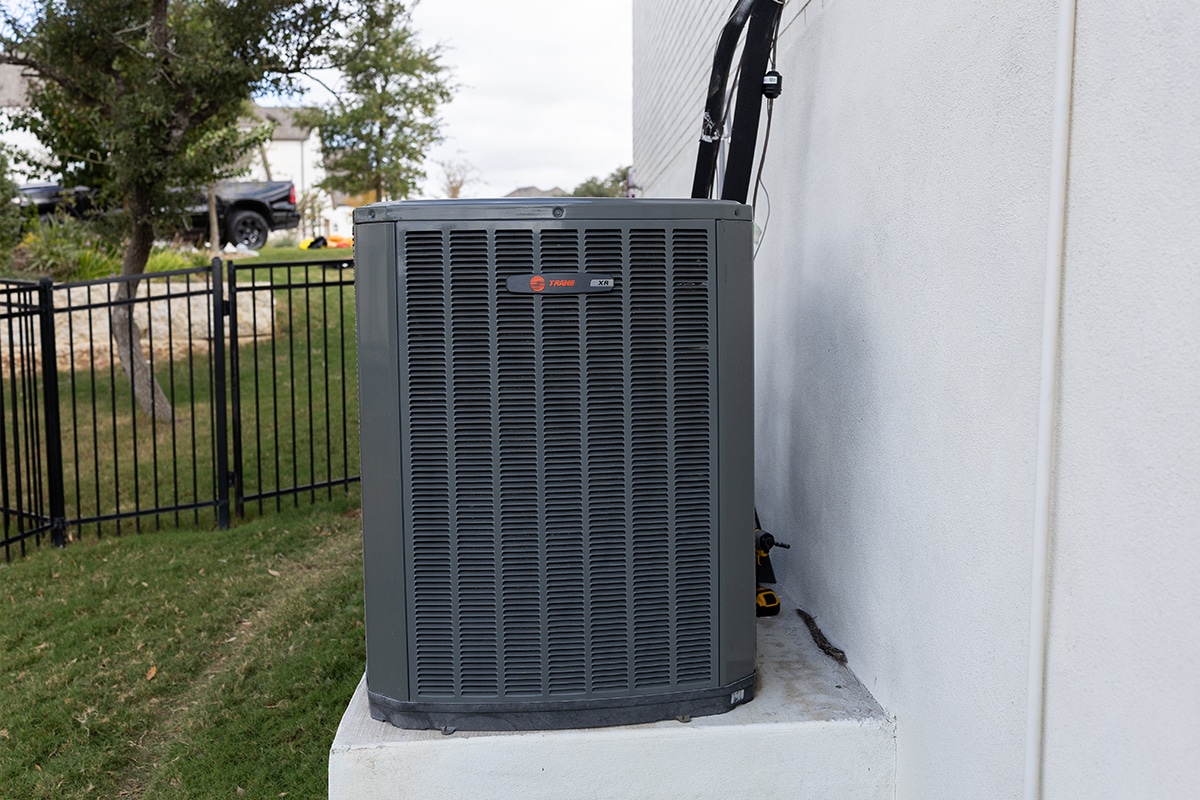 Trane XR outdoor air conditioning condenser unit installed on a concrete pad beside a residential home in San Antonio, TX