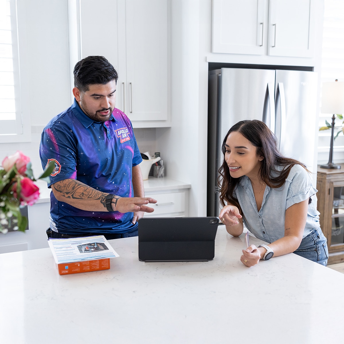 Apollo Air Heating and Cooling technician reviewing HVAC service options and pricing on a tablet with a homeowner at her kitchen counter in San Antonio