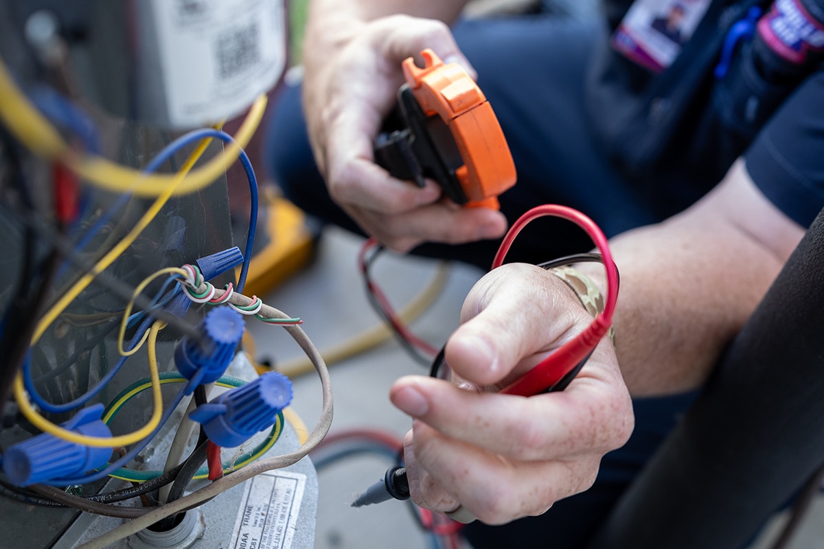 Apollo Air HVAC technician using a clamp meter to test electrical components and wiring on an outdoor AC condenser unit in San Antonio, TX