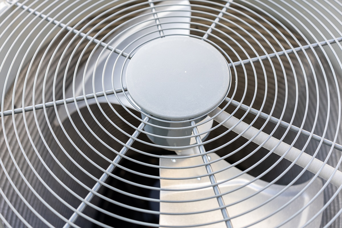 Close-up view of an outdoor air conditioner condenser unit fan with metal wire guard